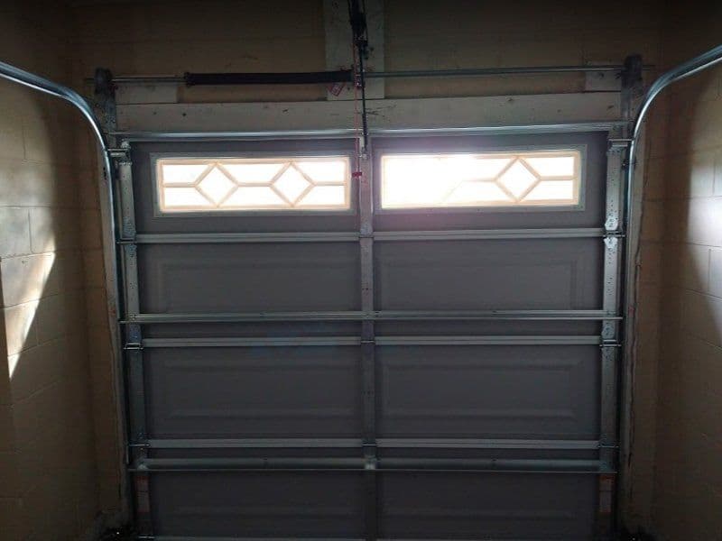 Garage door with decorative glass windows, closed and installed with metal tracks.