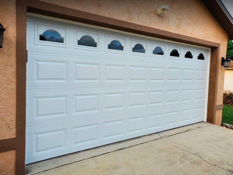White sectional garage door with decorative windows on top, installed on a home exterior.