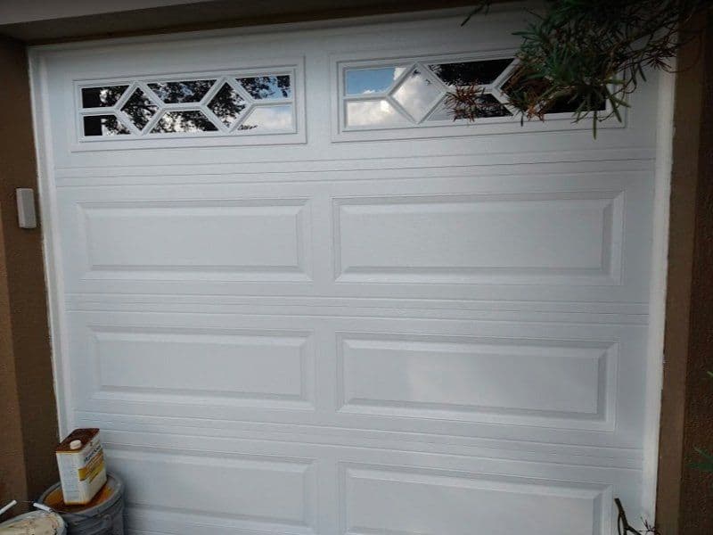 White garage door with decorative windows, modern design and textured panels.