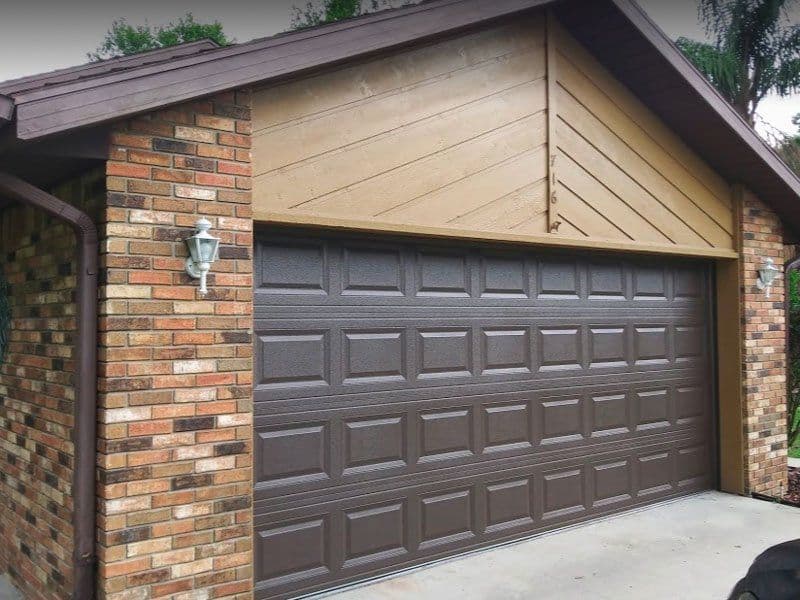 Brown garage door on brick house with a decorative light fixture and wooden accents.