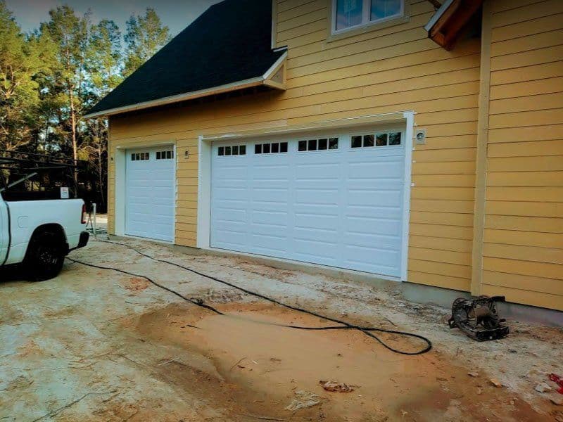 Newly constructed home with yellow siding, two white garage doors, and construction tools nearby.